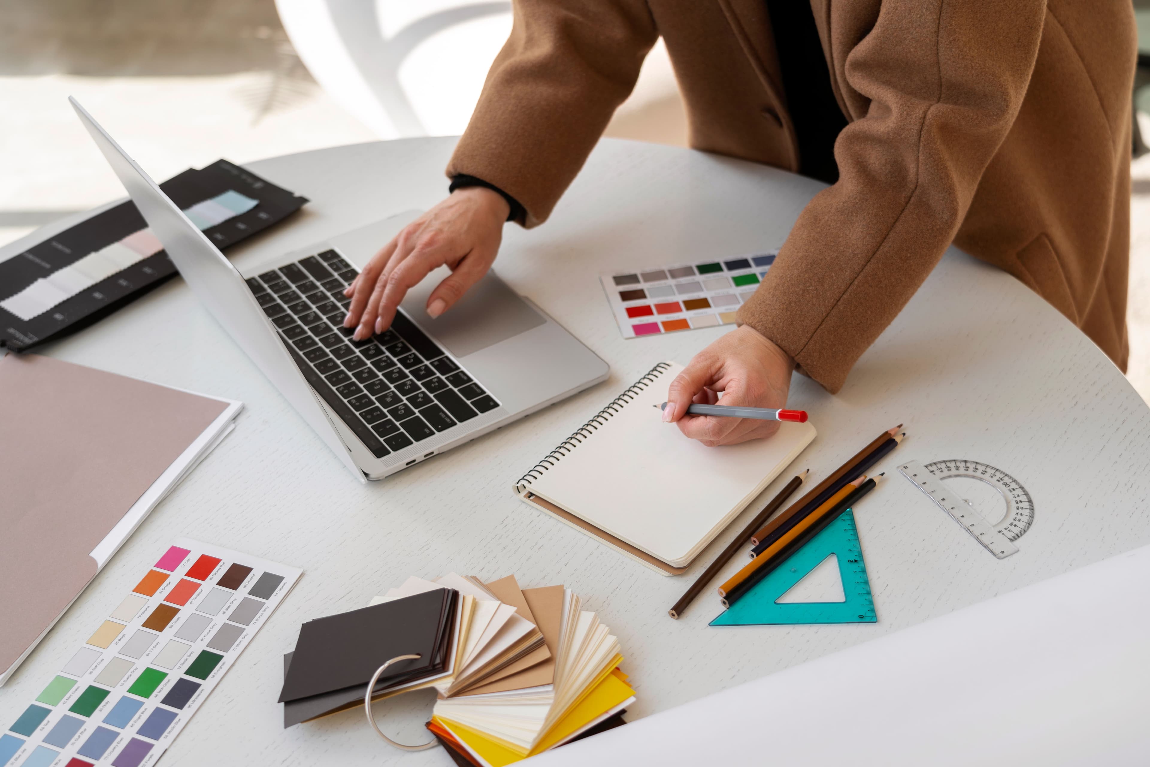una donna che progetta con computer, mazzette colori e righelli