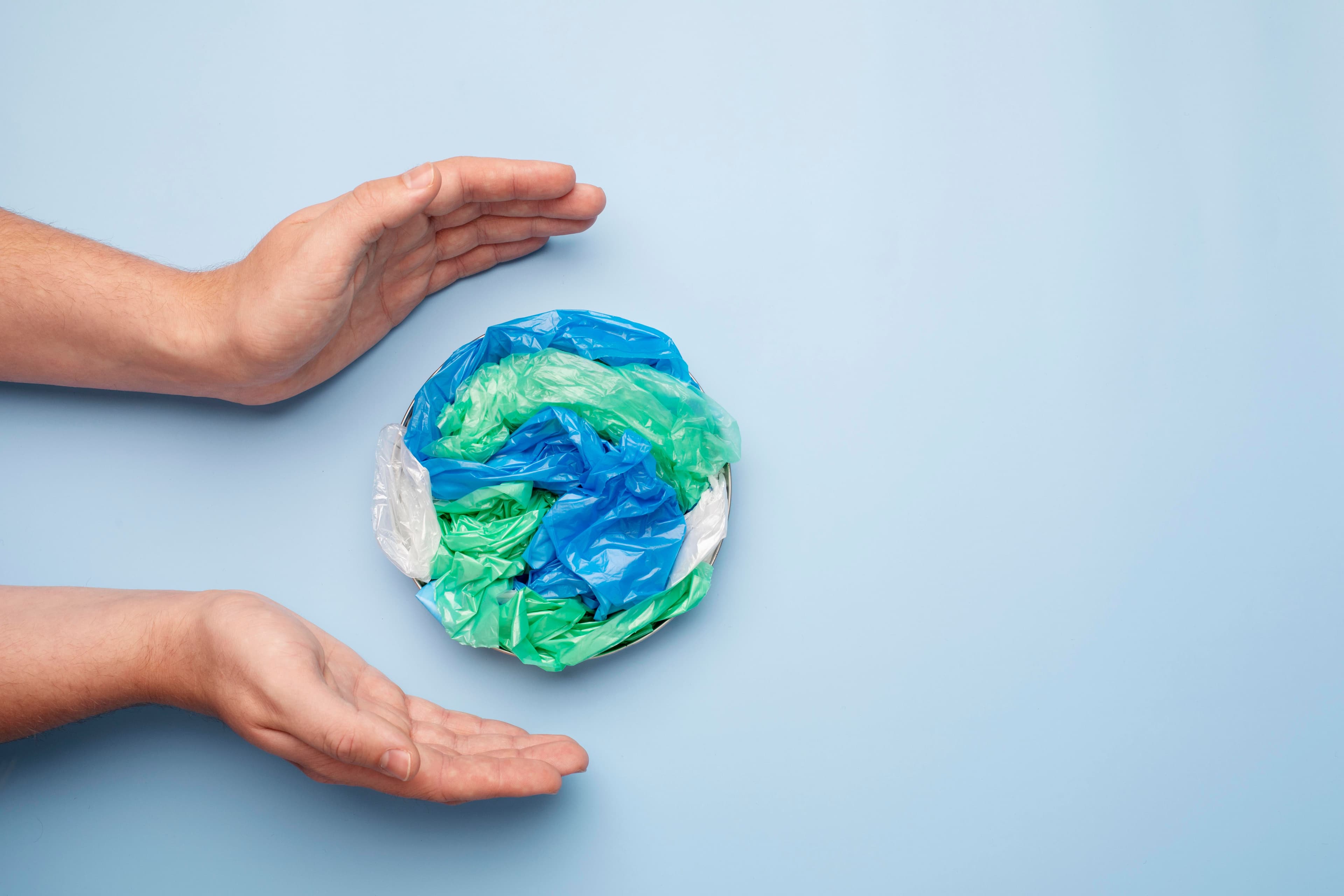 mani con un mondo fatto di plastica su fondo azzurro