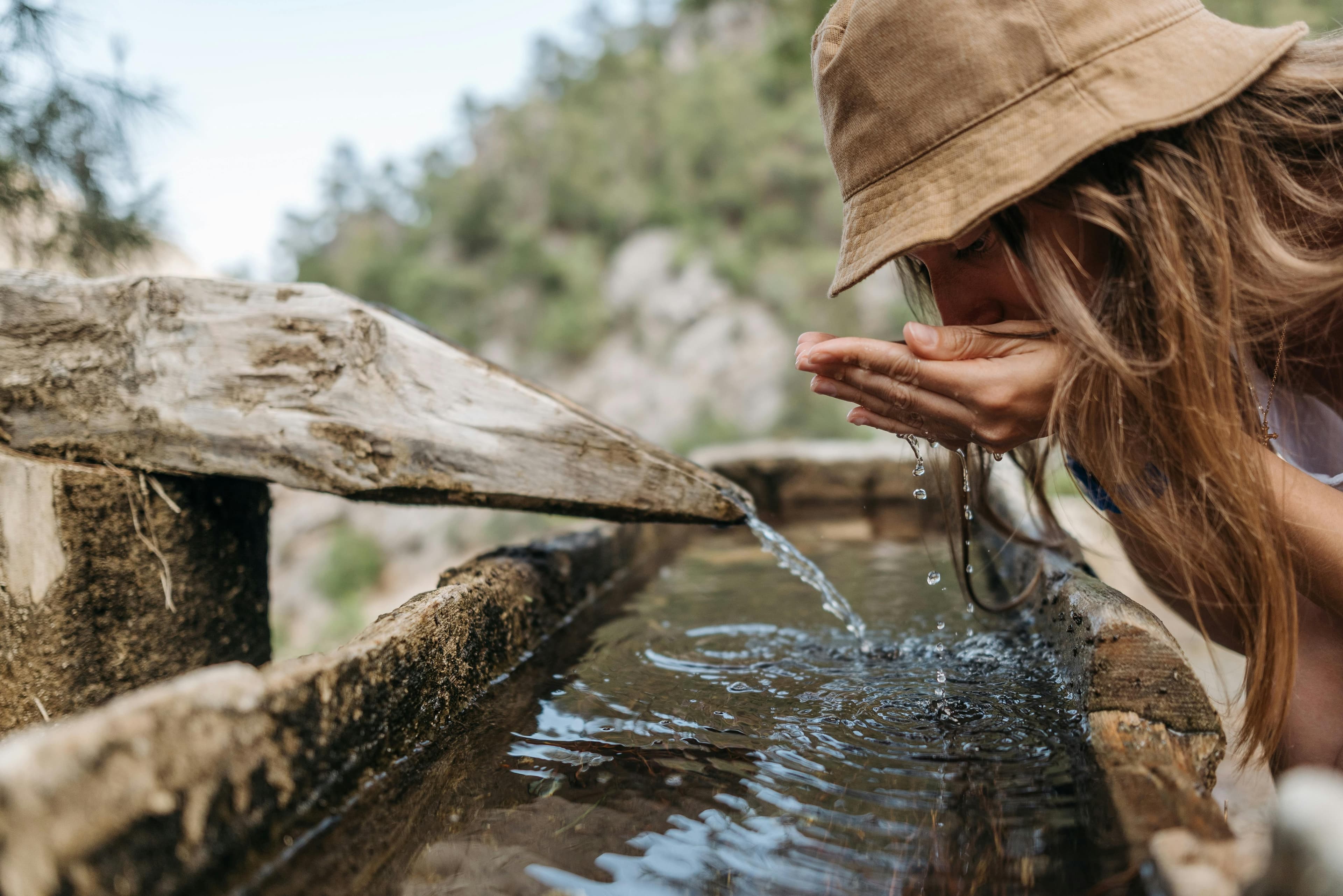 L'IMMAGINE RAPPRESENTA UNA DONNA CHE SI ABBEVERA AD UNA FONTANA IN UN CONTESTO NATURALE