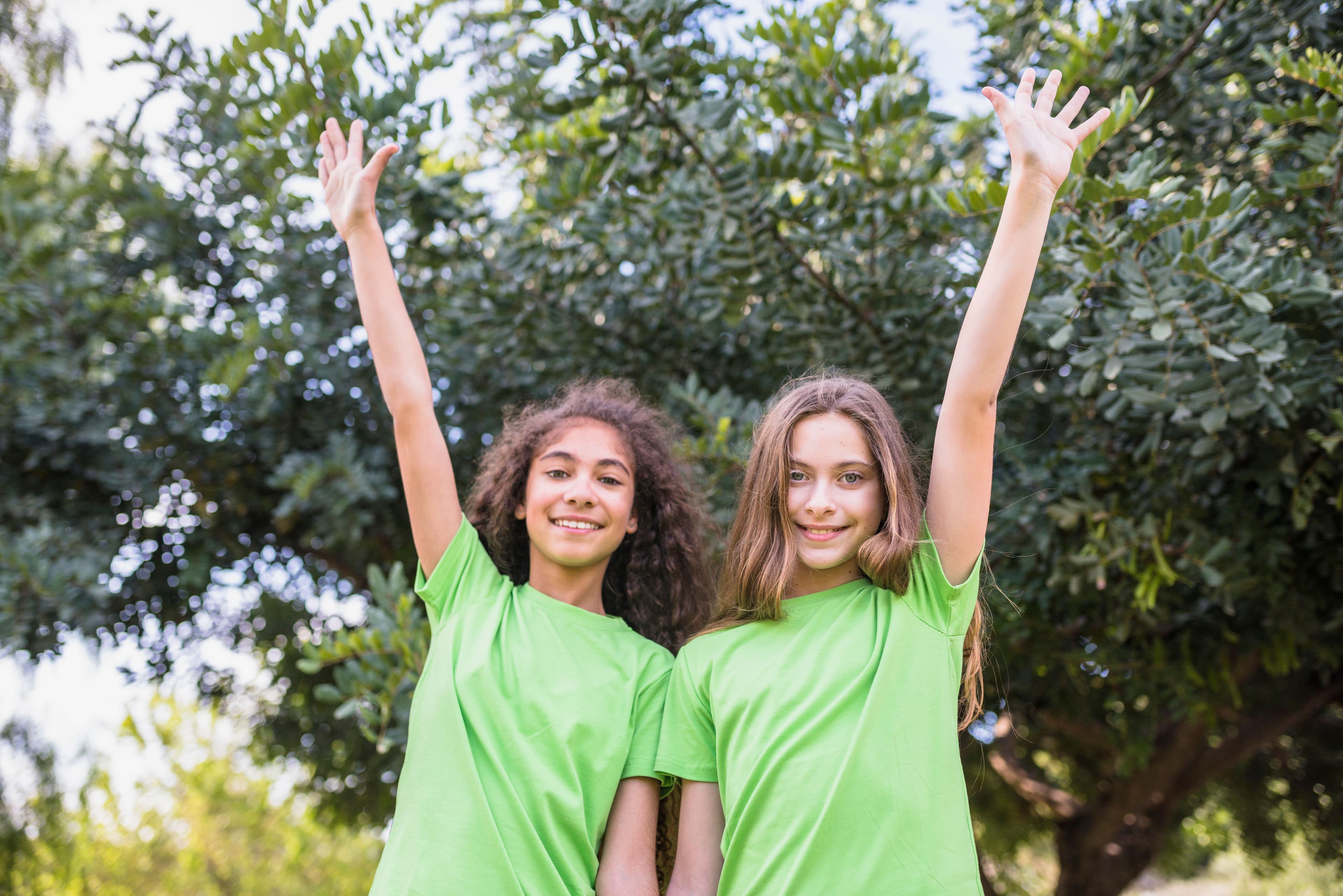 due bambine sorridenti con le magliette verdi con lo sfondo di alberi